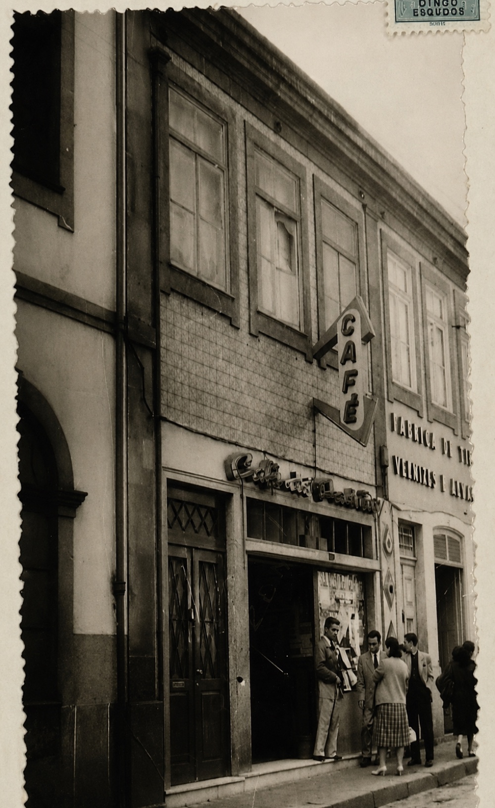 Historical postcard of the building's façade with its projecting CAFÉ sign and patrons at the door